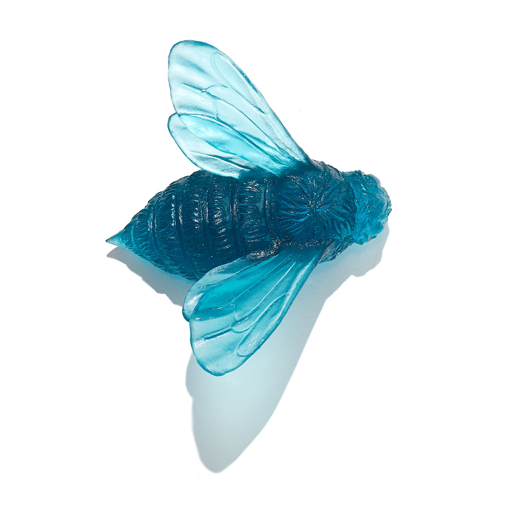 A translucent blue bee-shaped decorative object with detailed wings and a textured body, photographed on a clean white background with a soft shadow.