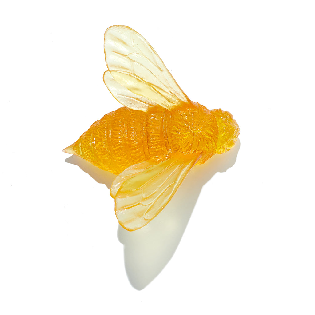 A yellow translucent glass bee with detailed wings and body, photographed on a clean white background with a soft shadow.