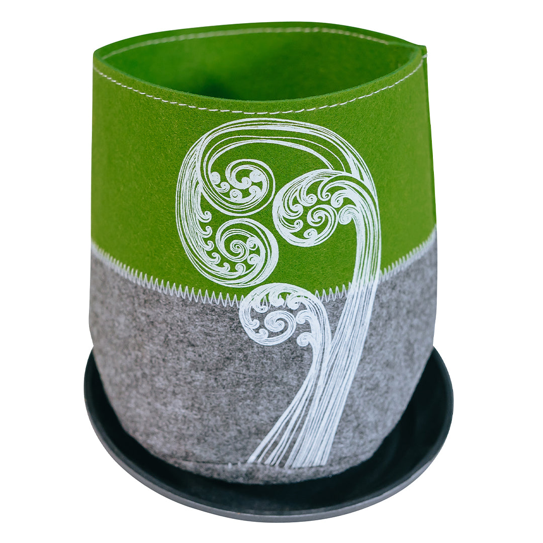A green and grey Ecofelt grow bag with a New Zealand native flora print, accompanied by a saucer. The bag is made from recycled plastic bottles and the saucer is made from biodegradable plant fibre.