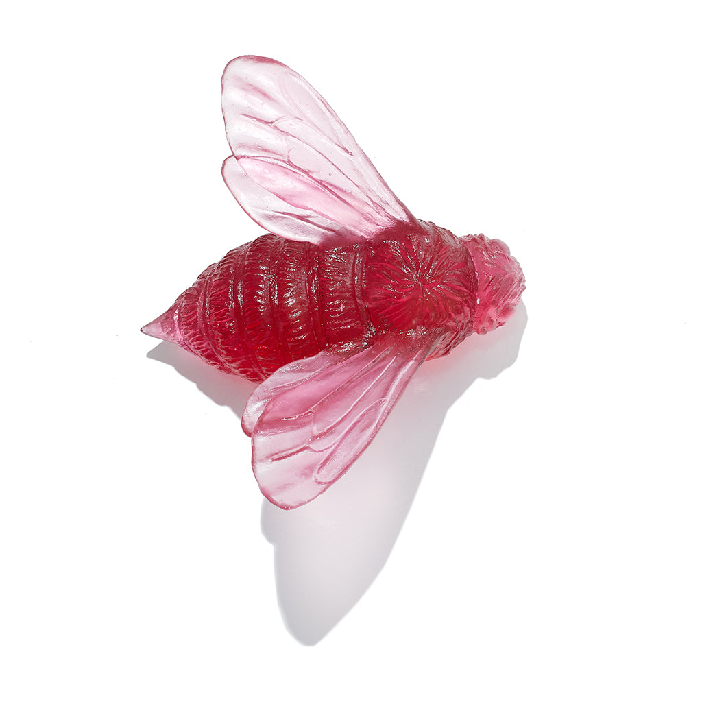 A translucent red bee-shaped decorative object with detailed wings and body, photographed on a clean white background with a soft shadow.