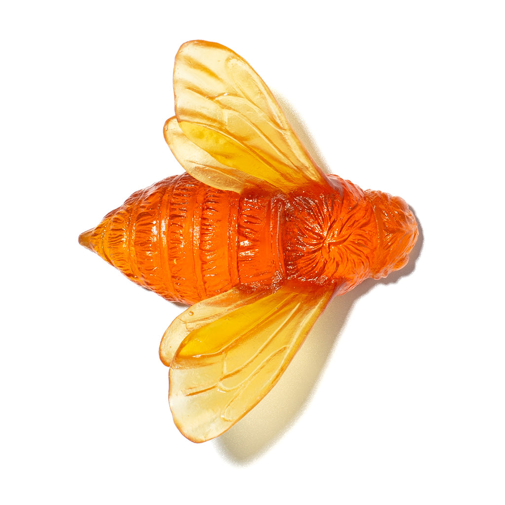 An amber-orange translucent glass bee sculpture with detailed wing and body textures, isolated on a white background.
