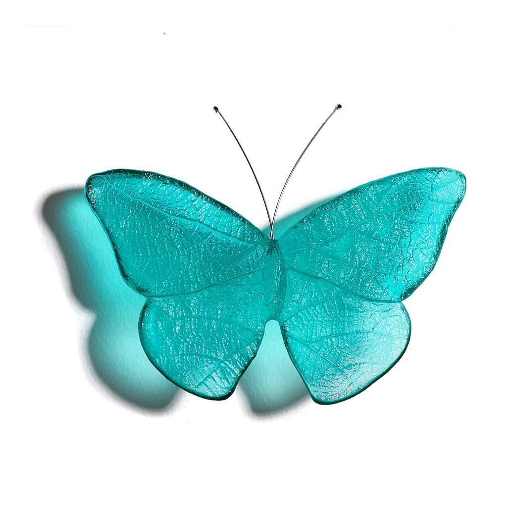 A translucent turquoise butterfly wall hanging with delicate wing veins and thin black antennae, shown against a plain white background with a soft shadow.