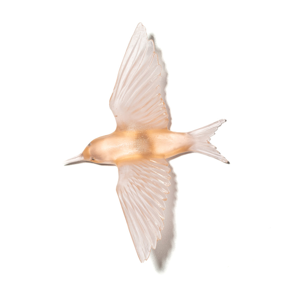 A translucent glass bird figurine in flight, featuring a warm peach body and delicate pale pink wings, isolated on a white background.