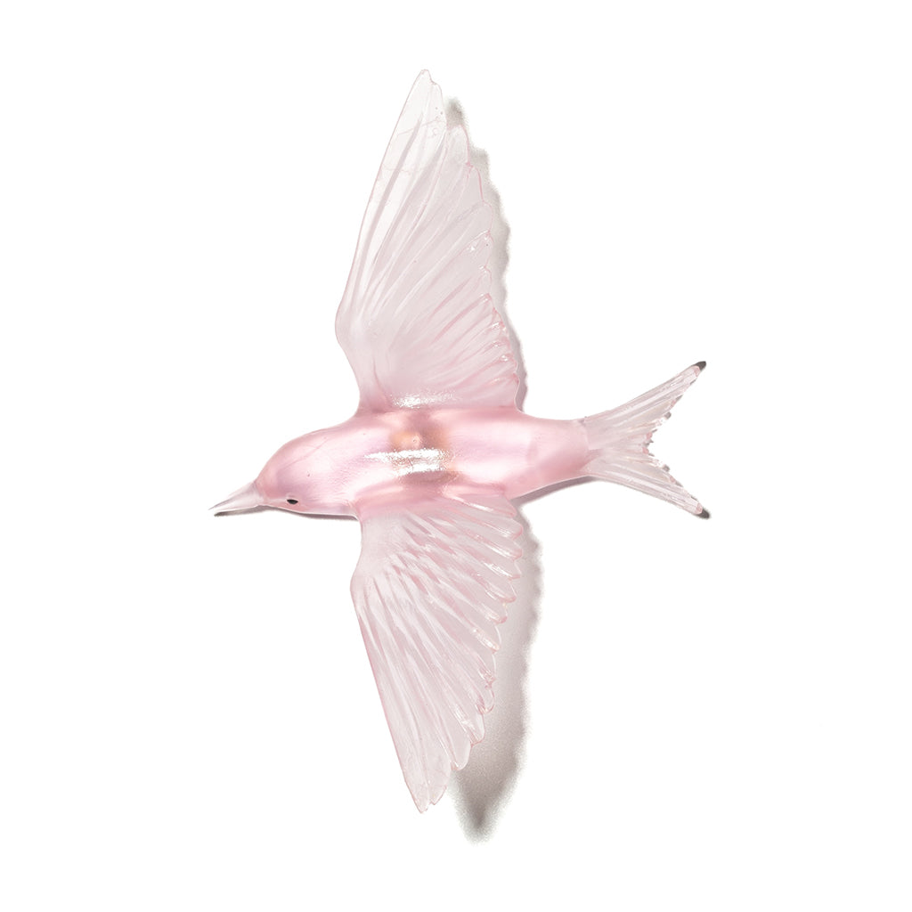 A translucent pink glass fairy tern bird figurine captured in flight against a solid white background.