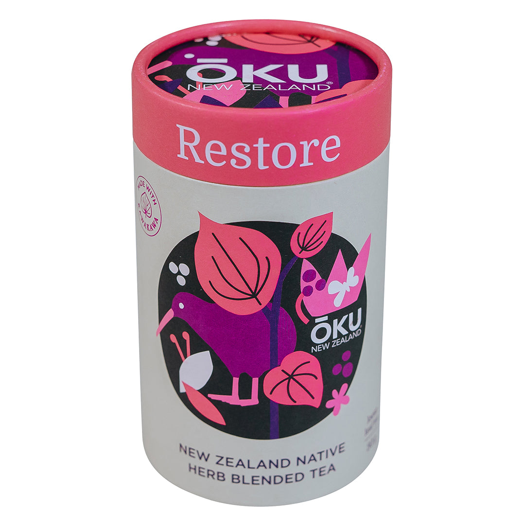 A cylindrical container of Oku Tea Restore with a pink lid, featuring illustrations of plants and the text 'NEW ZEALAND NATIVE HERB BLENDED TEA'.