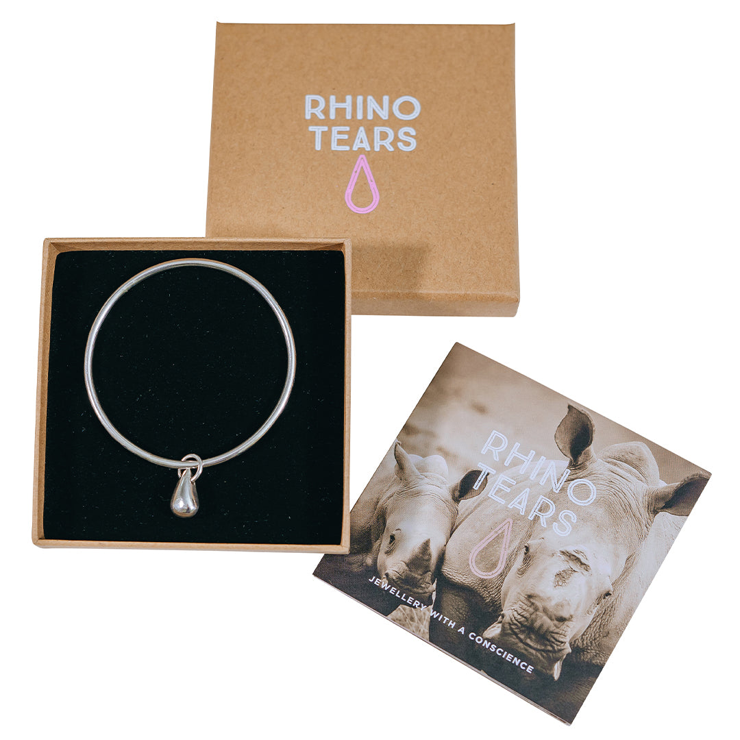 A silver bangle with a teardrop charm, presented in a box with 'RHINO TEARS' branding and a rhinoceros image. A conservation organization's card is also visible with rhinoceros imagery.