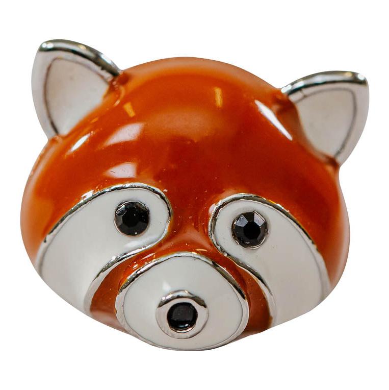 A red panda face shaped brooch made from hypoallergenic metal, with gem eyes, red and white enameling and a metallic finish.