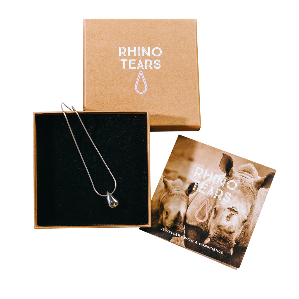 The image shows a silver tear-shaped pendant on a silver chain, presented in a branded box with 'RHINO TEARS' branding on the lid. There's also a card with information about the Rhino Tears collection.